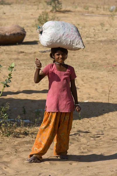 PUSHKAR, ÍNDIA - NOVEMBRO 18: Uma menina não identificada carregando um pacote na cabeça participa do Pushkar Camel Mela em 18 de novembro de 2012 em Pushkar, Rajastão, Índia . — Fotografia de Stock