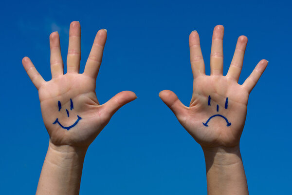 Hands with smiles and sadness pattern against the blue sky