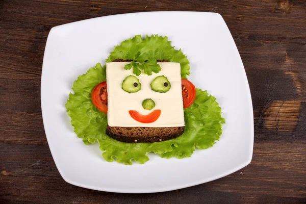 Веселая еда для детей - лицо на хлебе, сделанное из сыра, салата, помидоров, огурцов и перца . — стоковое фото