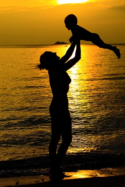 Moeder en haar kind silhouetten op strand bij zonsondergang — Stockfoto