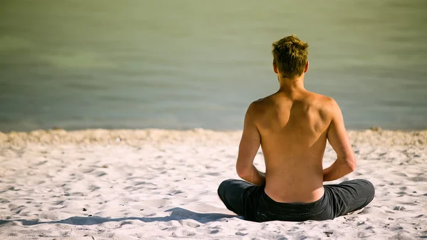 Sitting man doing yoga on shore of ocean — Stock Photo, Image