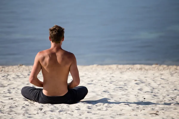 Uomo seduto che fa yoga sulla riva dell'oceano — Foto Stock