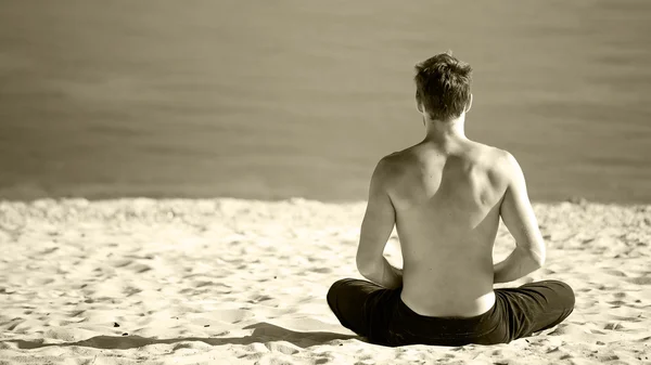 Hombre sentado haciendo yoga en la orilla del océano . —  Fotos de Stock