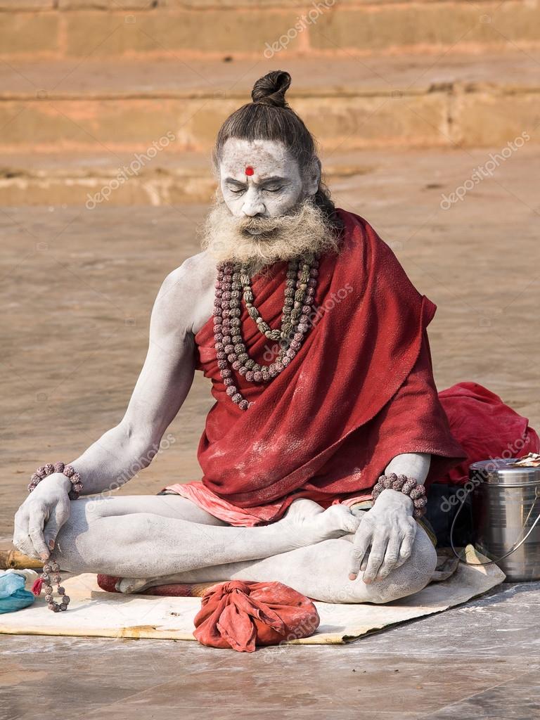 VARANASI, INDIA - DECEMBER 1, 2012 : An unidentified sadhu sits on the ghat along the Ganges river. Tourism has drawn many alleged fake sadhus to Varanasi
