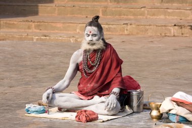 Sadhu sits on the ghat along the Ganges river in Varanasi, India. clipart