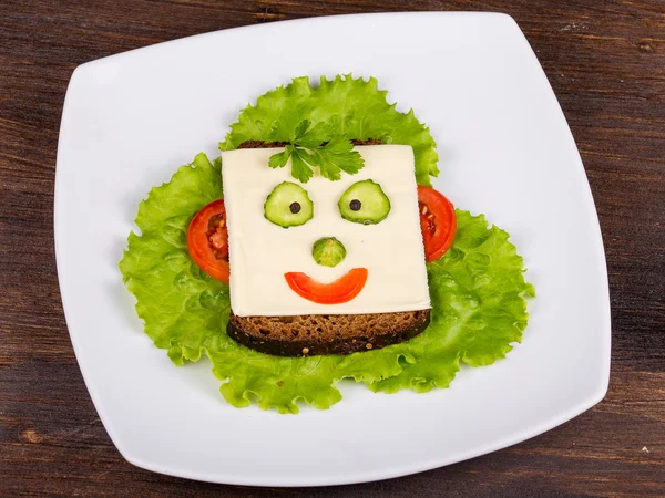 Лицо на хлеб, сделанный из сыра, салата, помидоров, огурцов и перца — стоковое фото
