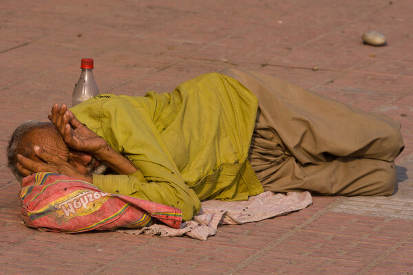 Homeless man sleeps on the sidewalk near the River Ganges in Haridwar, India.