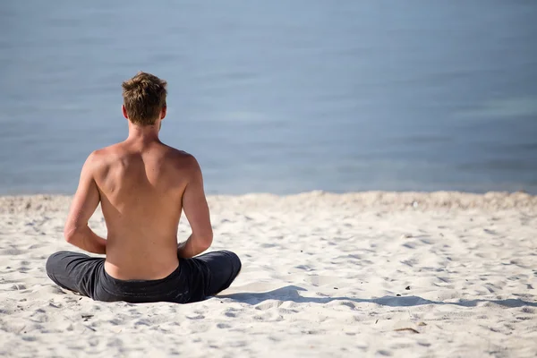 Uomo seduto che fa yoga sulla riva dell'oceano — Foto Stock