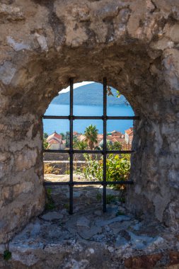 Herceg Novi şehri, mavi deniz manzarası ve Karadağ 'daki kalenin taş duvarında ızgarası olan bir delikten geçen binalar. Güzel Boka Kotorska Koyu 'nun girişinde yer alan kasaba.
