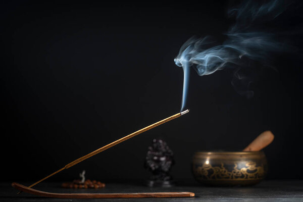 Asian incense stick in stick holder burning with smoke on black background, close up, copy space. Meditation, yoga, self development and sound therapy concept