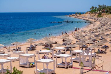 Sharm El Sheikh, Mısır - 28 Mayıs 2021: İnsanlar Sharm El Sheikh, Mısır, Afrika 'daki Kızıldeniz kıyısındaki bir tropik tatil beldesinde plaj sandalyeleri ve saman şemsiyeleriyle lüks bir kumsalda dinleniyorlar.