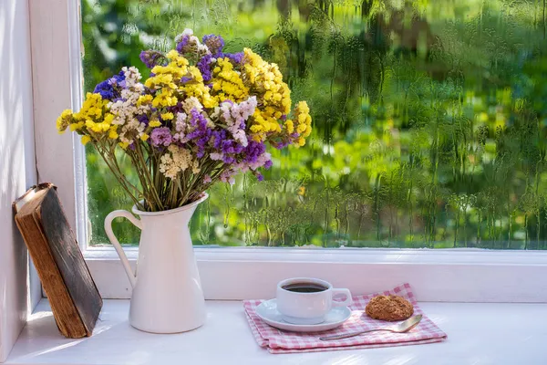 庭の近くの夏の日に自宅で雨滴と窓の背景に花やコーヒーの白いカップの古い本 カラフルな花束 コピースペース — ストック写真