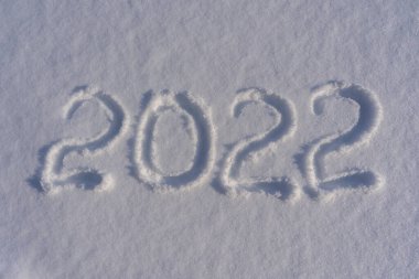 Yeni yılın kutlu olsun 2022. Karlı kış arkaplanına karşı gelecek yılın sembolü olarak kar yüzeyine karla yazılmış sayılar. 2022 yazıtları güneş ışığında kar yığınında. Yeni Yıl