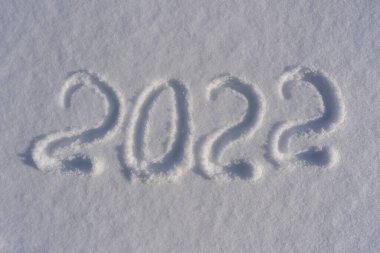 Yeni yılın kutlu olsun 2022. Karlı kış arkaplanına karşı gelecek yılın sembolü olarak kar yüzeyine karla yazılmış sayılar. 2022 yazıtları güneş ışığında kar yığınında. Yeni Yıl