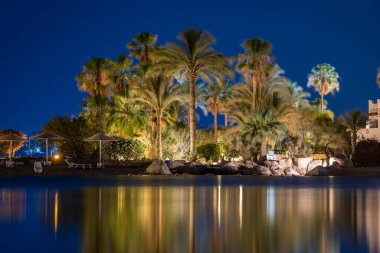 Binalar, güneş panelleri ve şemsiyeler Mısır 'ın Sharm El Sheikh tatil beldesindeki kumsaldaki sakin deniz suyuna yansıtılır.