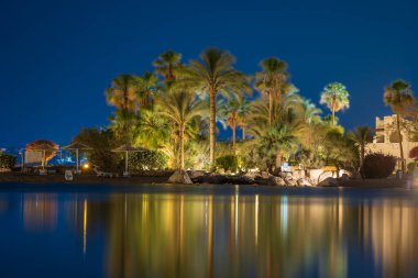 Binalar, güneş panelleri ve şemsiyeler Mısır 'ın Sharm El Sheikh tatil beldesindeki kumsaldaki sakin deniz suyuna yansıtılır.
