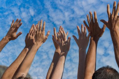 Bir grup insan mavi gökyüzünde beyaz bulutlarla el kaldırıyor.