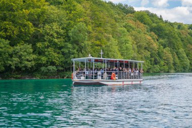 Plitvice Gölleri, Hırvatistan - 30 Ağustos 2021: İnsanlar yaz aylarında Hırvatistan, Orta Avrupa, seyahat ve doğa kavramları ile Plitvice Gölleri kıyıları boyunca turistik bir tekneye biniyor