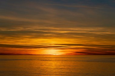 Güneş batarken deniz suyu yüzeyi olan görkemli bir manzara. Bulutlar ve deniz suyuyla gün batımı gökyüzü