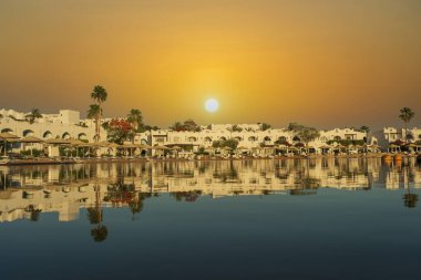 Binalar, güneş panelleri ve şemsiyeler, sabah Sharm El Sheikh 'in sahil kasabasındaki sakin deniz suyuna yansıtılır.