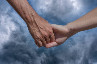 Karanlık gökyüzünde, bulutlu arka planda iki el bir arada, yakın çekim.