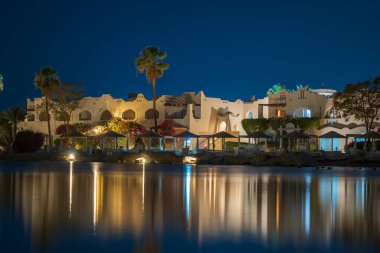 Binalar, güneş panelleri ve şemsiyeler Mısır 'ın Sharm El Sheikh tatil beldesindeki kumsaldaki sakin deniz suyuna yansıtılır.