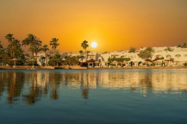 Binalar, güneş panelleri ve şemsiyeler, sabah Sharm El Sheikh 'in sahil kasabasındaki sakin deniz suyuna yansıtılır.