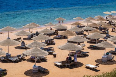 Sharm El Sheikh, Mısır - 28 Mayıs 2021: İnsanlar Sharm El Sheikh, Mısır, Afrika 'daki Kızıldeniz kıyısındaki bir tropik tatil beldesinde plaj sandalyeleri ve saman şemsiyeleriyle lüks bir kumsalda dinleniyorlar.