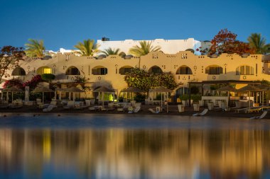 Binalar, güneş panelleri ve şemsiyeler Mısır 'ın Sharm El Sheikh tatil beldesindeki kumsaldaki sakin deniz suyuna yansıtılır.