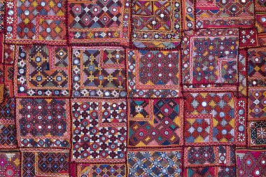 Hindistan 'ın arka planındaki renkli halının detaylarını anlat. Bir tuvale dikilmiş çeşitli kumaş parçalarını kapat