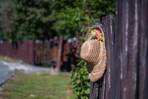 人工の花を持つ古いわらの帽子は ハンガリー ヨーロッパ クローズアップのホロコの民族誌的村の通りの木製の柵にかかっています — ストック写真