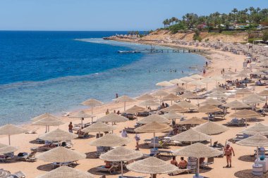 Sharm El Sheikh, Mısır - 25 Mayıs 2021: İnsanlar Sharm El Sheikh, Mısır, Afrika 'daki Kızıldeniz kıyısındaki bir tropik tatil beldesinde plaj sandalyeleri ve saman şemsiyeleriyle lüks bir kumsalda dinleniyorlar.