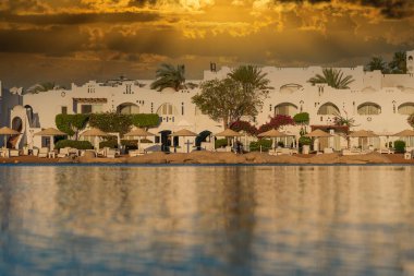 Binalar, güneş panelleri ve şemsiyeler, sabah Sharm El Sheikh 'in sahil kasabasındaki sakin deniz suyuna yansıtılır.