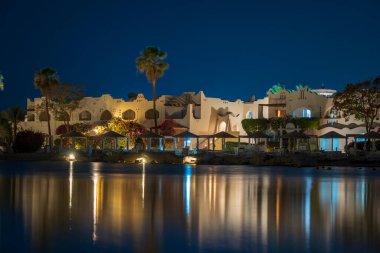 Binalar, güneş panelleri ve şemsiyeler Mısır 'ın Sharm El Sheikh tatil beldesindeki kumsaldaki sakin deniz suyuna yansıtılır.