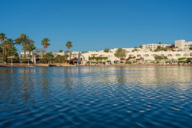 Gündoğumunda, Mısır 'ın Sharm El Sheikh tatil beldesindeki sakin deniz suyuna binalar, güneşlikler ve şemsiyeler yansıtılır.
