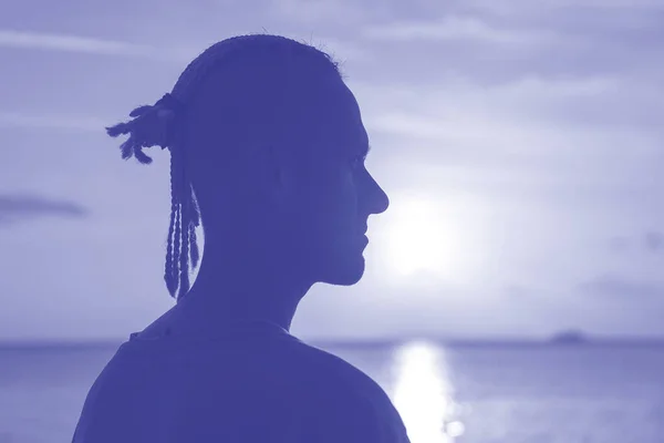 日没時に海の近くの頭の上にドレッドロックを持つ若い男のシルエット 2022年のトレンドカラー 写真のウルトラバイオレットクリエイティブとムーディーカラー — ストック写真
