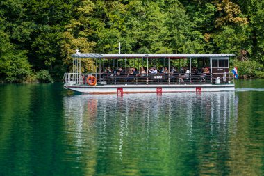 Plitvice Gölleri, Hırvatistan - 30 Ağustos 2021: İnsanlar yaz aylarında Hırvatistan, Orta Avrupa, seyahat ve doğa kavramları ile Plitvice Gölleri kıyıları boyunca turistik bir tekneye biniyor