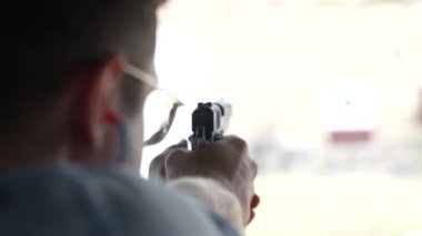 Bir adam atış poligonundaki hedeflere silahla ateş ediyor, yakın çekim, bulanık odak. Eğitimde, ağır çekimde, hedefe ateş eden bir adamın arka görüntüsü.