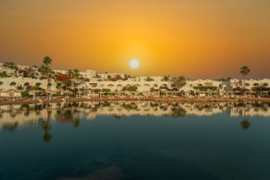Binalar, güneş panelleri ve şemsiyeler, sabah Sharm El Sheikh 'in sahil kasabasındaki sakin deniz suyuna yansıtılır.