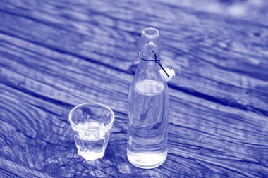 Ahşap masanın üzerinde su olan şişe ve cam, yakın çekim. 2022 yılının moda rengi. Filmin Ultra Violet yaratıcı ve karamsar rengi