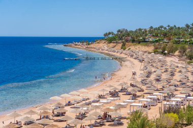 Sharm El Sheikh, Mısır - 25 Mayıs 2021: İnsanlar Sharm El Sheikh, Mısır, Afrika 'daki Kızıldeniz kıyısındaki bir tropik tatil beldesinde plaj sandalyeleri ve saman şemsiyeleriyle lüks bir kumsalda dinleniyorlar.