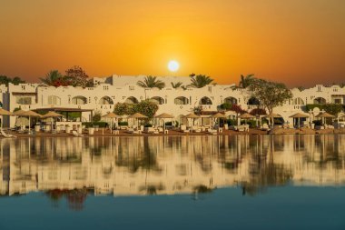 Binalar, güneş panelleri ve şemsiyeler, sabah Sharm El Sheikh 'in sahil kasabasındaki sakin deniz suyuna yansıtılır.