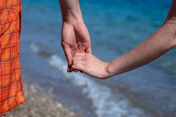 ビーチの背景に青い海の水の近くで一緒に開催されたカップルの手を閉じる — ストック写真