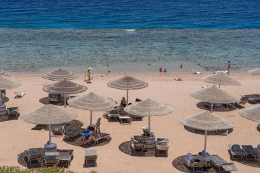 Sharm El Sheikh, Mısır - 25 Mayıs 2021: İnsanlar Sharm El Sheikh, Mısır, Afrika 'daki Kızıldeniz kıyısındaki bir tropik tatil beldesinde plaj sandalyeleri ve saman şemsiyeleriyle lüks bir kumsalda dinleniyorlar.