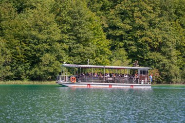 Plitvice Gölleri, Hırvatistan - 30 Ağustos 2021: İnsanlar yaz aylarında Hırvatistan, Orta Avrupa, seyahat ve doğa kavramları ile Plitvice Gölleri kıyıları boyunca turistik bir tekneye biniyor