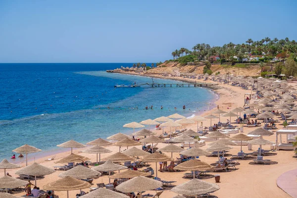 Sharm El Sheikh, Mısır - 28 Mayıs 2021: İnsanlar Sharm El Sheikh, Mısır, Afrika 'daki Kızıldeniz kıyısındaki bir tropik tatil beldesinde plaj sandalyeleri ve saman şemsiyeleriyle lüks bir kumsalda dinleniyorlar.
