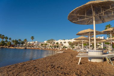 Lüks kumsalda plaj sandalyeleri ve beyaz hasır şemsiyelerle Sharm El Sheikh, Mısır, Afrika 'daki Kızıldeniz kıyısındaki tropikal tatil beldesinde. Karantina sırasında boş plajlar