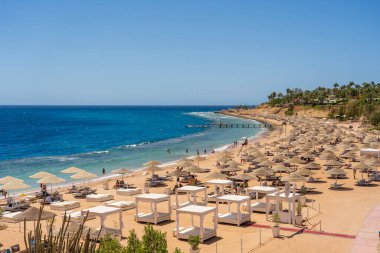 Sharm El Sheikh, Mısır - 23 Mayıs 2021: İnsanlar Sharm El Sheikh, Mısır, Afrika 'daki Kızıldeniz kıyısındaki bir tropik tatil beldesinde plaj sandalyeleri ve saman şemsiyeleriyle lüks bir kumsalda dinleniyorlar.