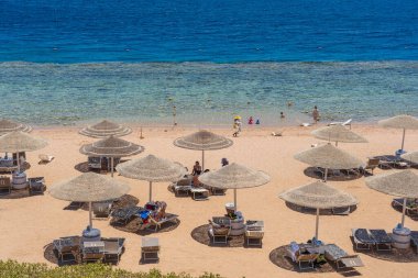 Sharm El Sheikh, Mısır - 25 Mayıs 2021: İnsanlar Sharm El Sheikh, Mısır, Afrika 'daki Kızıldeniz kıyısındaki bir tropik tatil beldesinde plaj sandalyeleri ve saman şemsiyeleriyle lüks bir kumsalda dinleniyorlar.