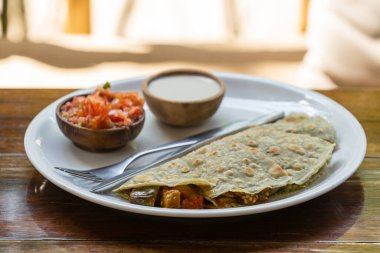 Spiral tortilla peynirli, patlıcanlı, domatesli, ekşi kremalı ve domates soslu Quesadilla tropikal kafe Tayland 'da ahşap masada, yakın plan, geleneksel Meksika çerezi